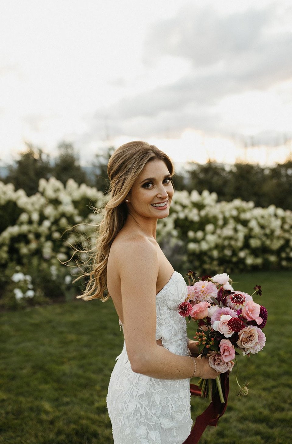The bride with a half-up and half-down hairstyle looking over her should hold a bouquet. 