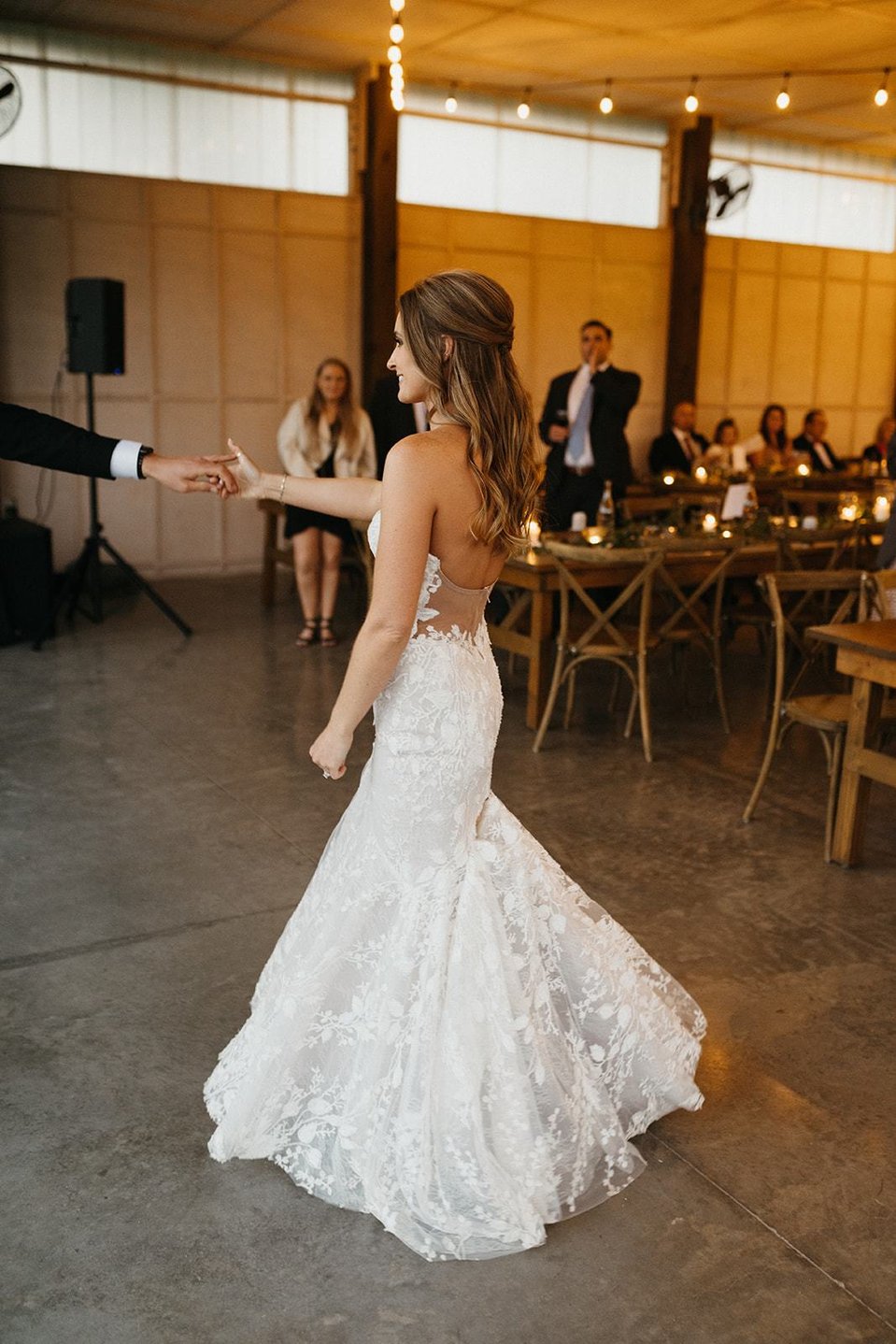 The bride with soft wavy wedding hairstyle holding groom's hand on the dance floor.