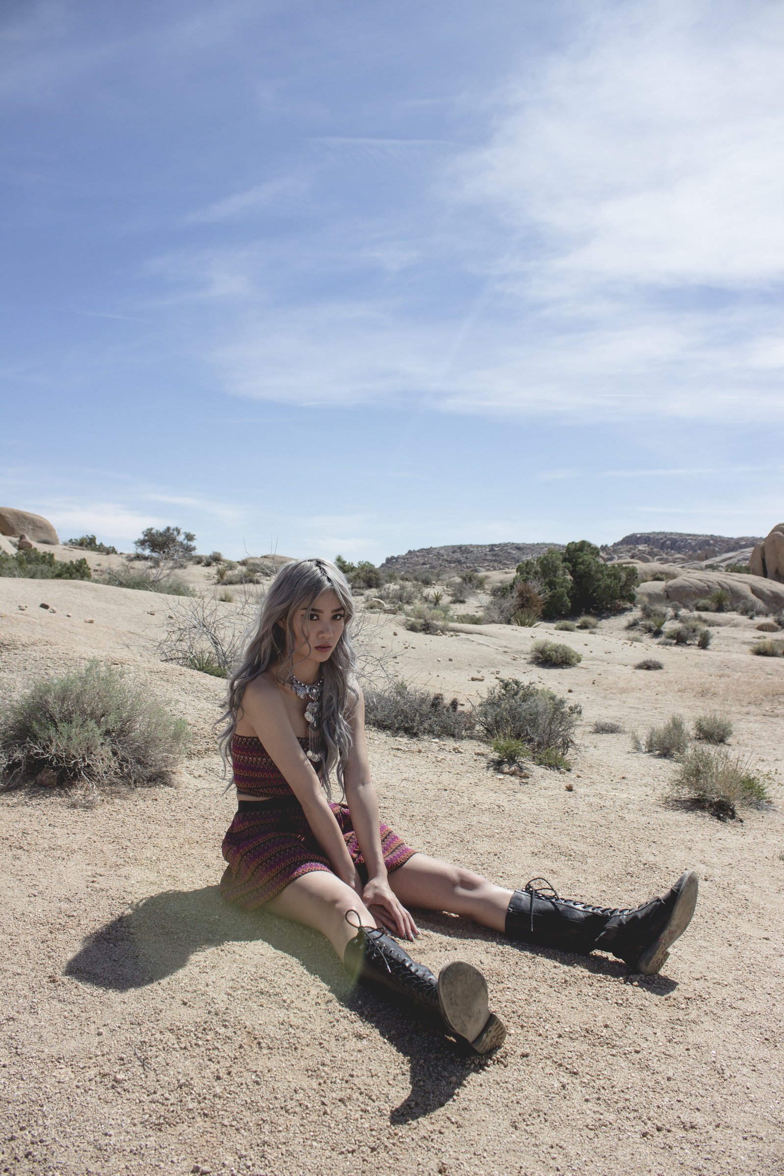Woman sitting on ground wearing dress and boots with desert and blue sky behind
