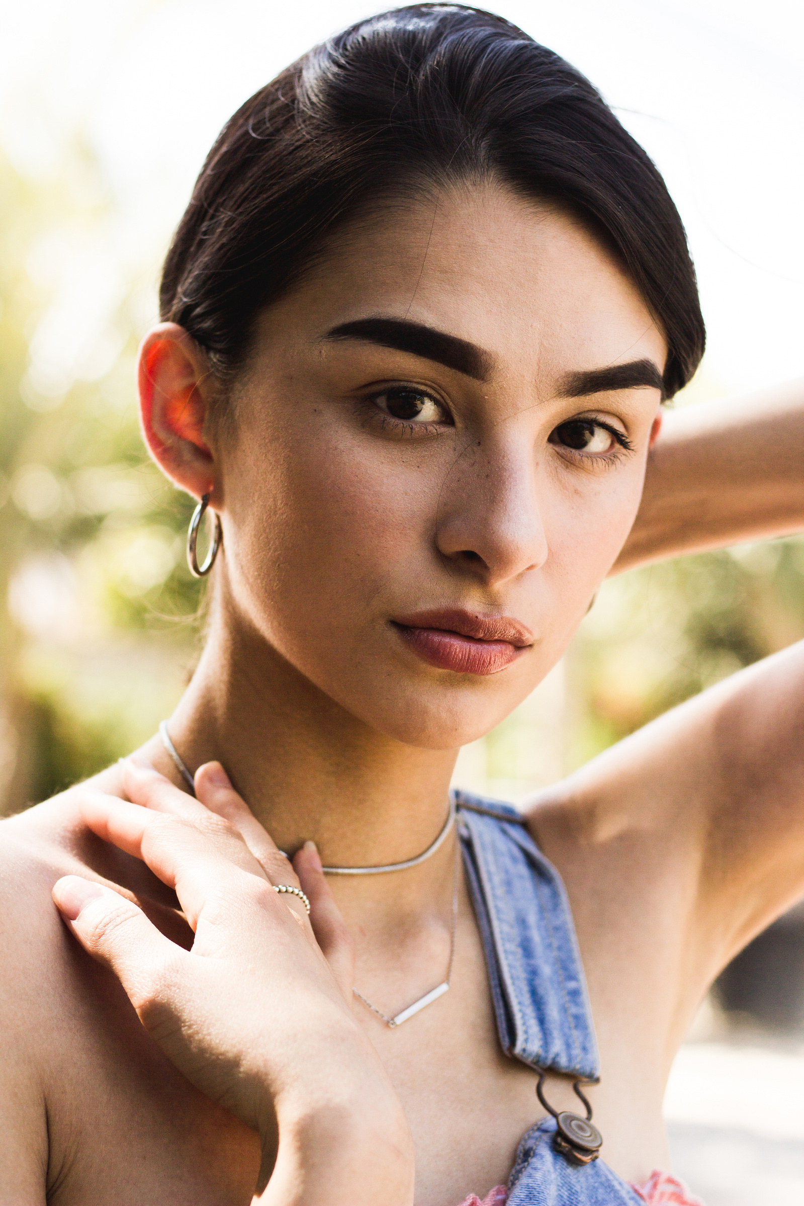 Woman standing in overalls, wearing jewelry with greenery behind
