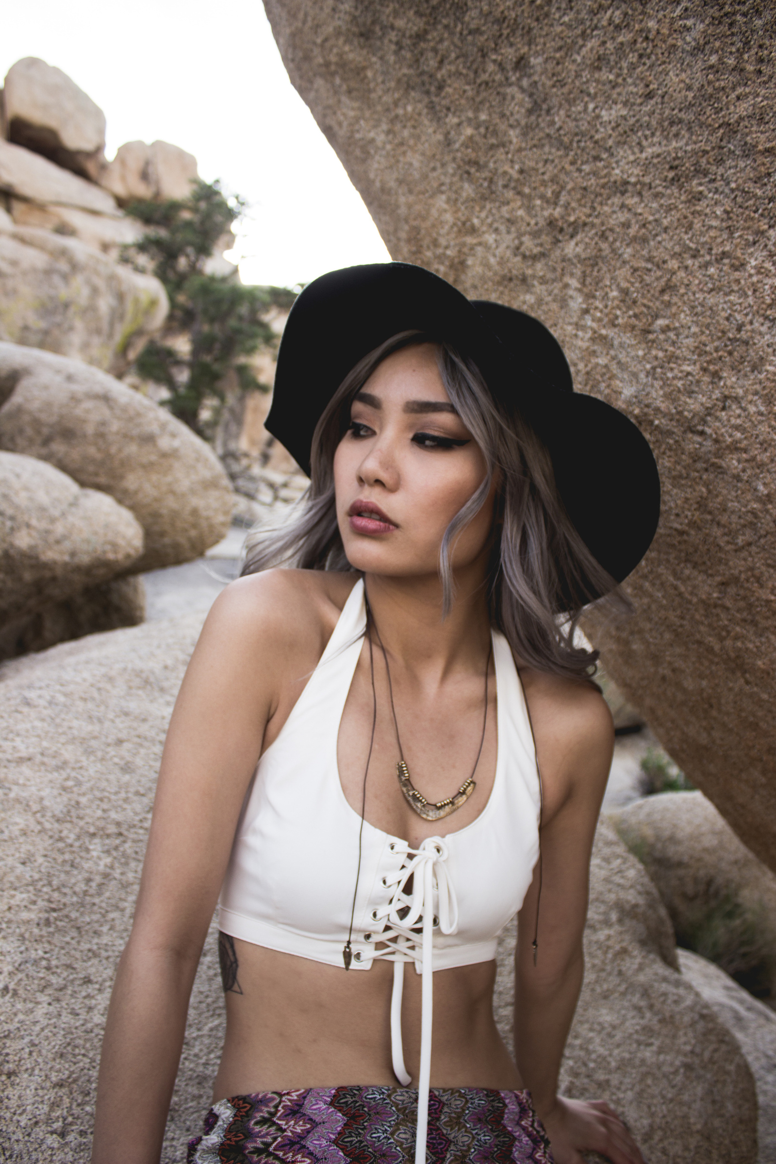 Woman wearing white top, jewelry and black hat with rock formation behind
