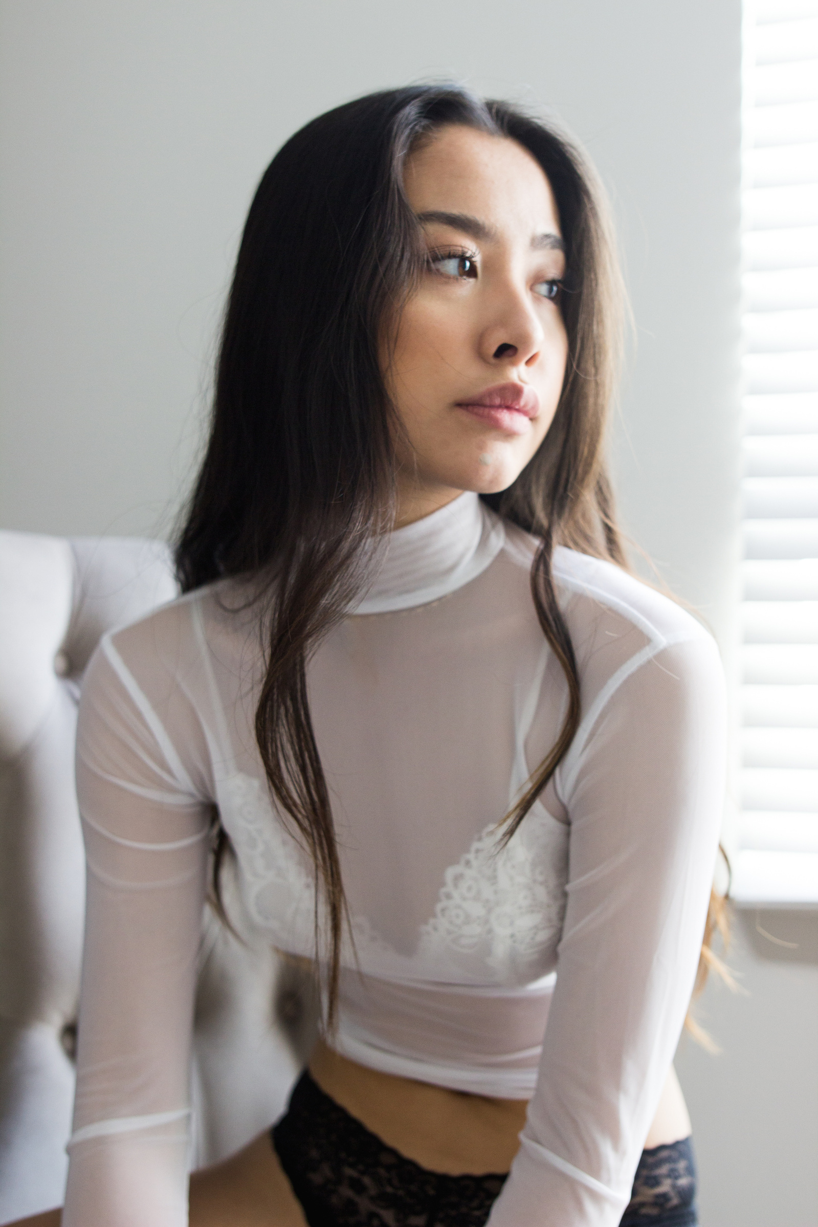 Woman wearing a white turtleneck top, sitting with sunlight through window behind