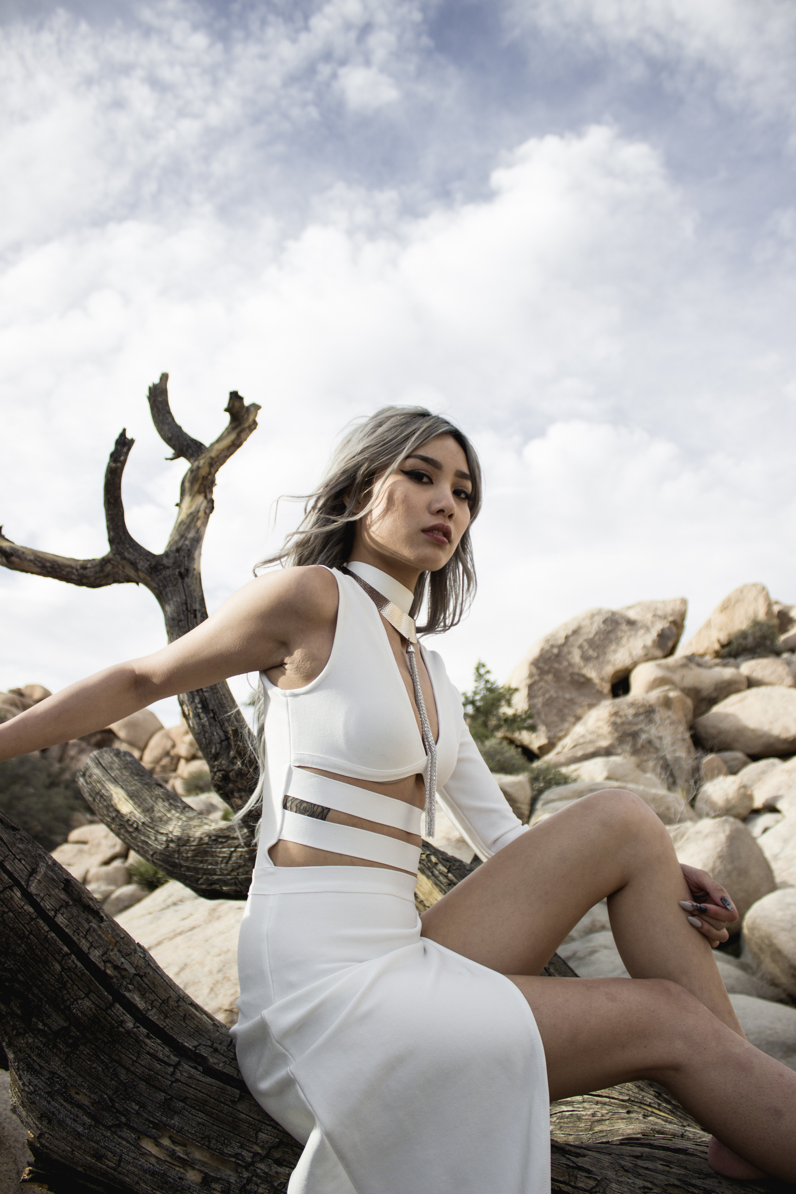 Woman sitting on tree with sky and rock formation behind