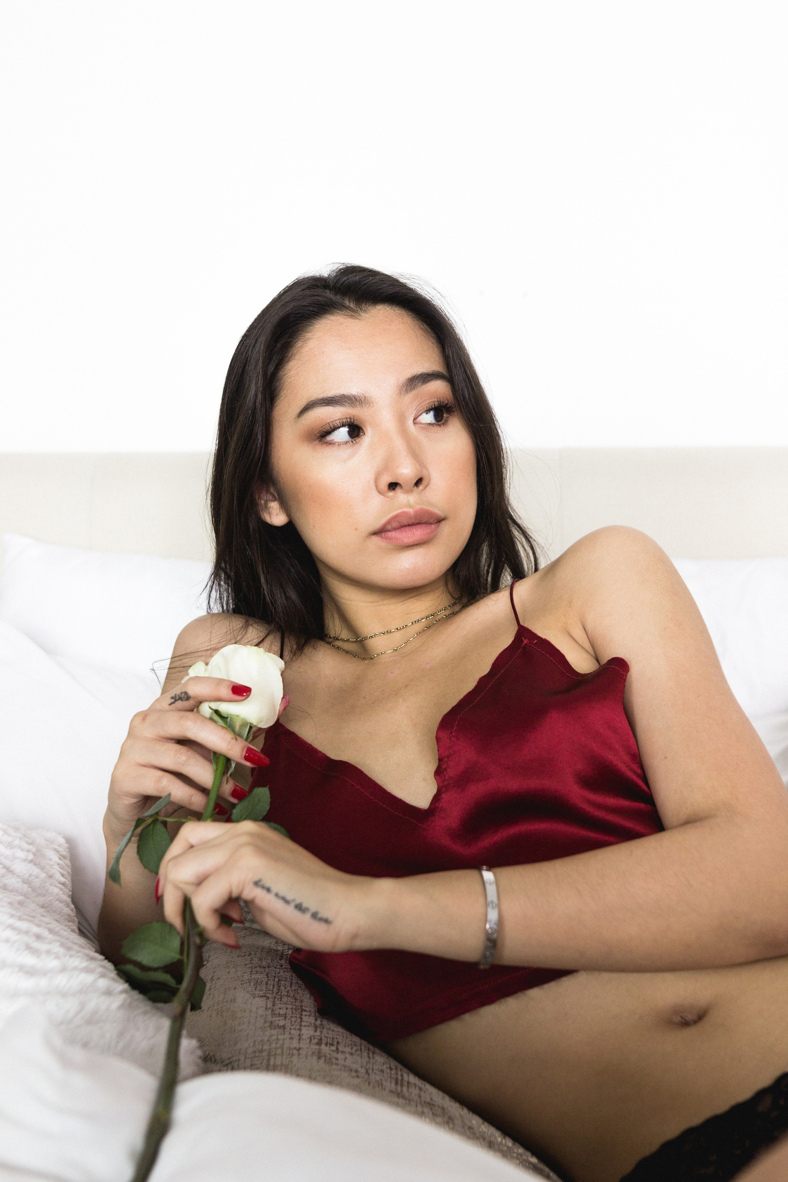 Woman sitting on bed, wearing a red top and holding a rose