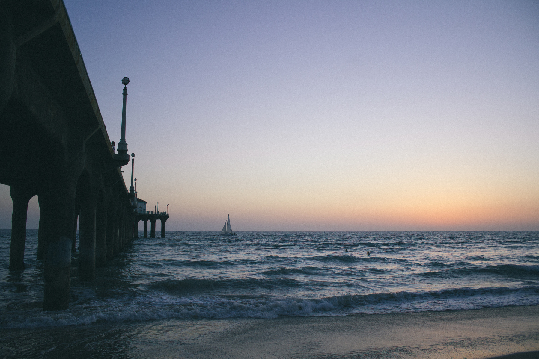 Boat in distance on top of the ocean next to beach pier with sky behind