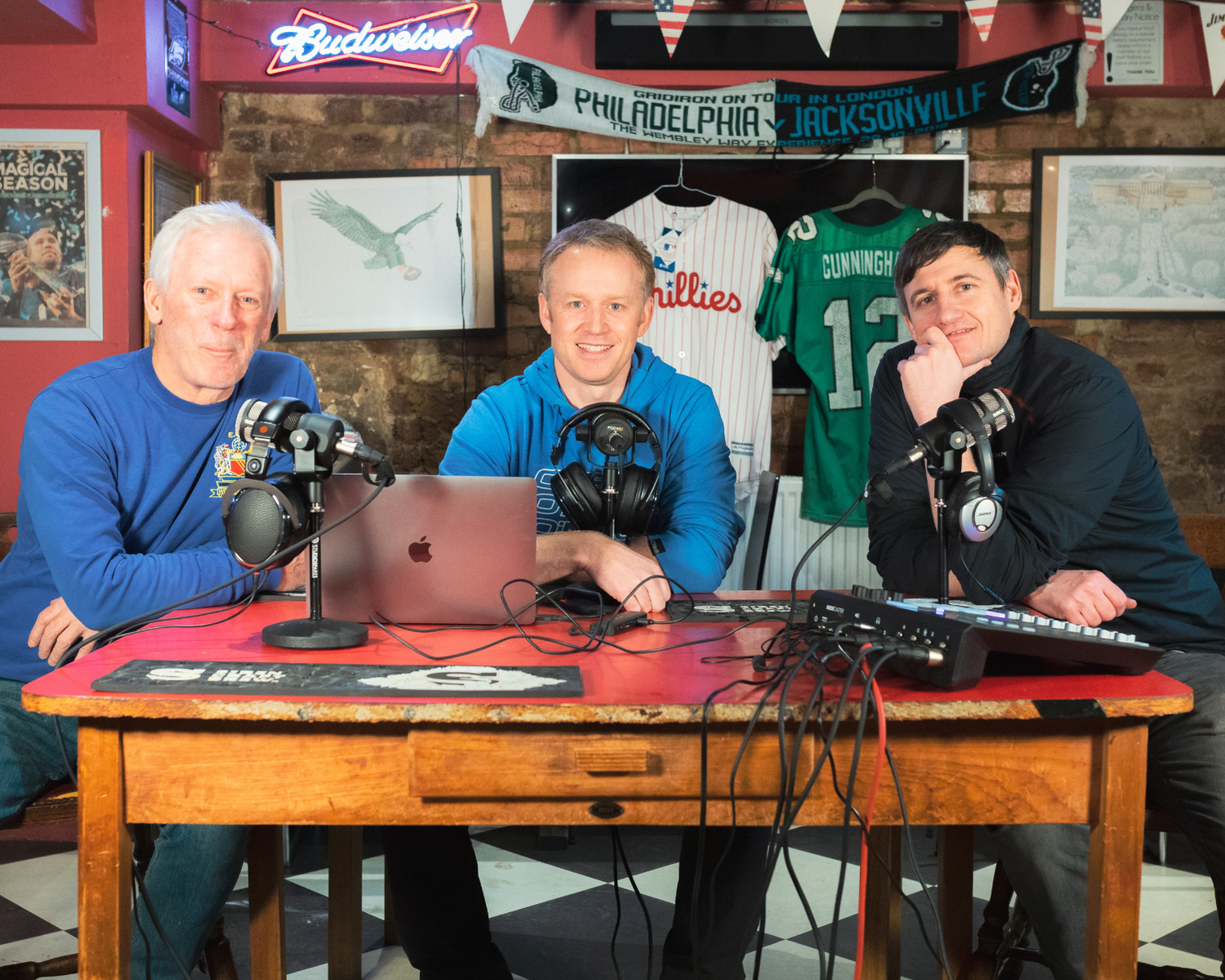 three men sat at a desk recording a podcast.