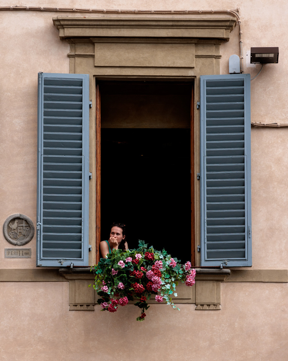 Person looking out of an open window, with blue shutters in Florence .