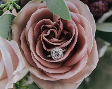 A beautiful engagement ring sits inside a mauve rose. 