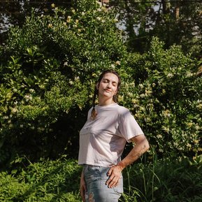 Rachel stands in my Delaware County backyard among overgrown foliage, enjoying the feel of the sun on her face. Her eyes are closed and her face is lit by warm, July sun.