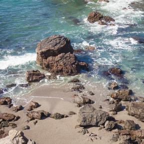 An overhead photograph of the Pacific Ocean and coastline, featuring rocky shores, sand, and the bluest water I've ever personally witnessed. 