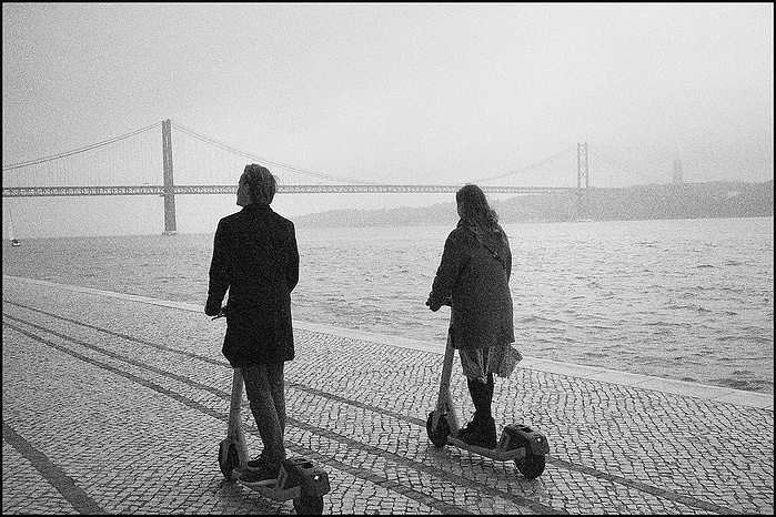 A couple on scooters with 25th April Bridge suspension The Ponte 25 de Abril in the background