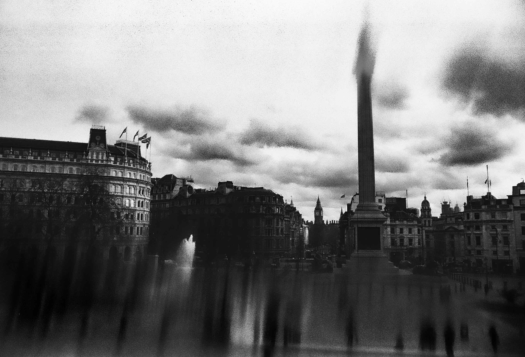 Black and white image taken from the national portrait gallery of a cloudy day at trafalgar square with nelson's column in the middle. 