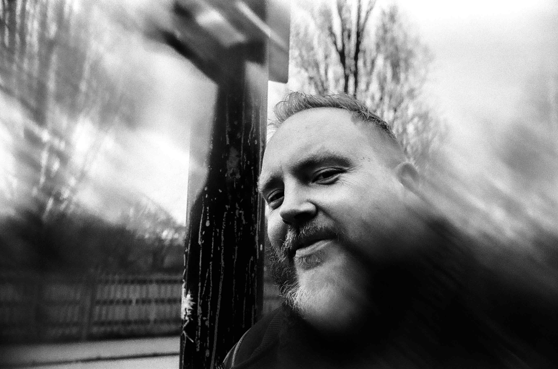 Black and white image of a bearded man leaning on a lamp-post on Endymion road in Haringey.