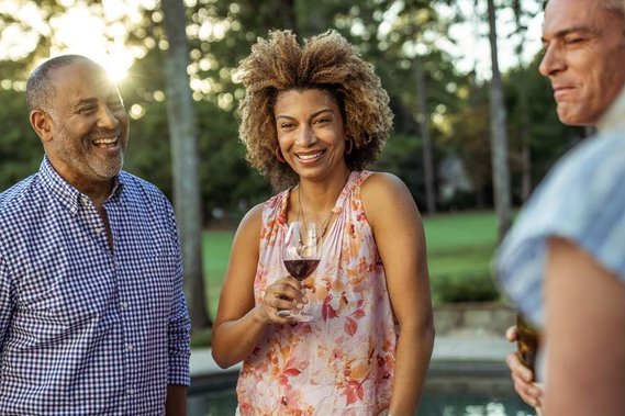 light-skinned black woman with afro curly hair standing with people outside in a backyard drinking red wine