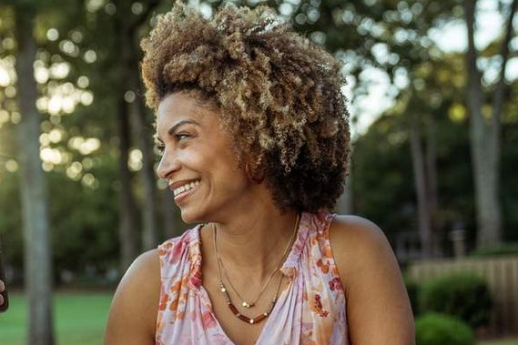 light-skinned black woman with afro curly hair standing outside near trees