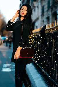 Jeune femme élégante qui pose Avenue Montaigne à Paris devant une grille aux flèches dorées
