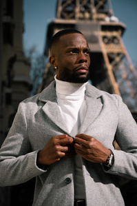 Jeune homme black très élégant qui pose en col roulé blanc et veste grise devant la Tour Eiffel à Paris