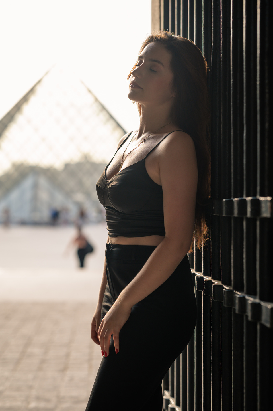 Jeune femme adossée à une grille avec la Pyramide du Louvre en arrière-plan