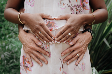 Mains d'un couple mixte formant un cœur sur le ventre de la jeune femme qui attend un enfant