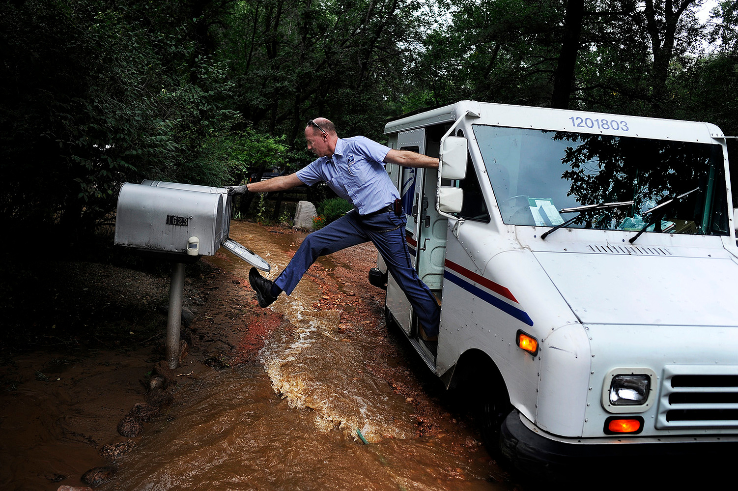 Dave Jackson closes a mailbox with his foot after delivering the mail to a home surrounded on three sides by a flooded Cheyenne Creek Friday, September 13, 2013. Seventeen counties in Colorado were affected by the floods that stretched from Colorado Spri