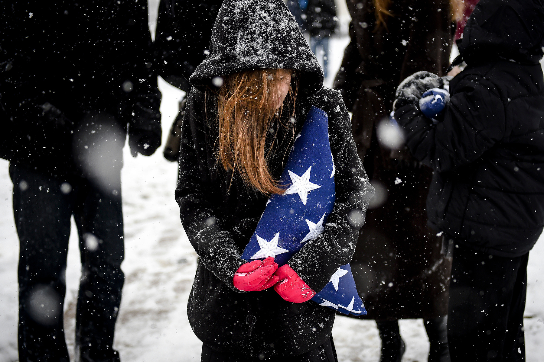 Katie Baylett, 9, grasps onto a folded flag as heavy snow falls after a Veterans Day memorial service for her father, retired Special Forces soldier Randall Baylett, 45, Tuesday, November 11, 2014 at the Memorial Park Veterans Memorial. Baylett, who passe