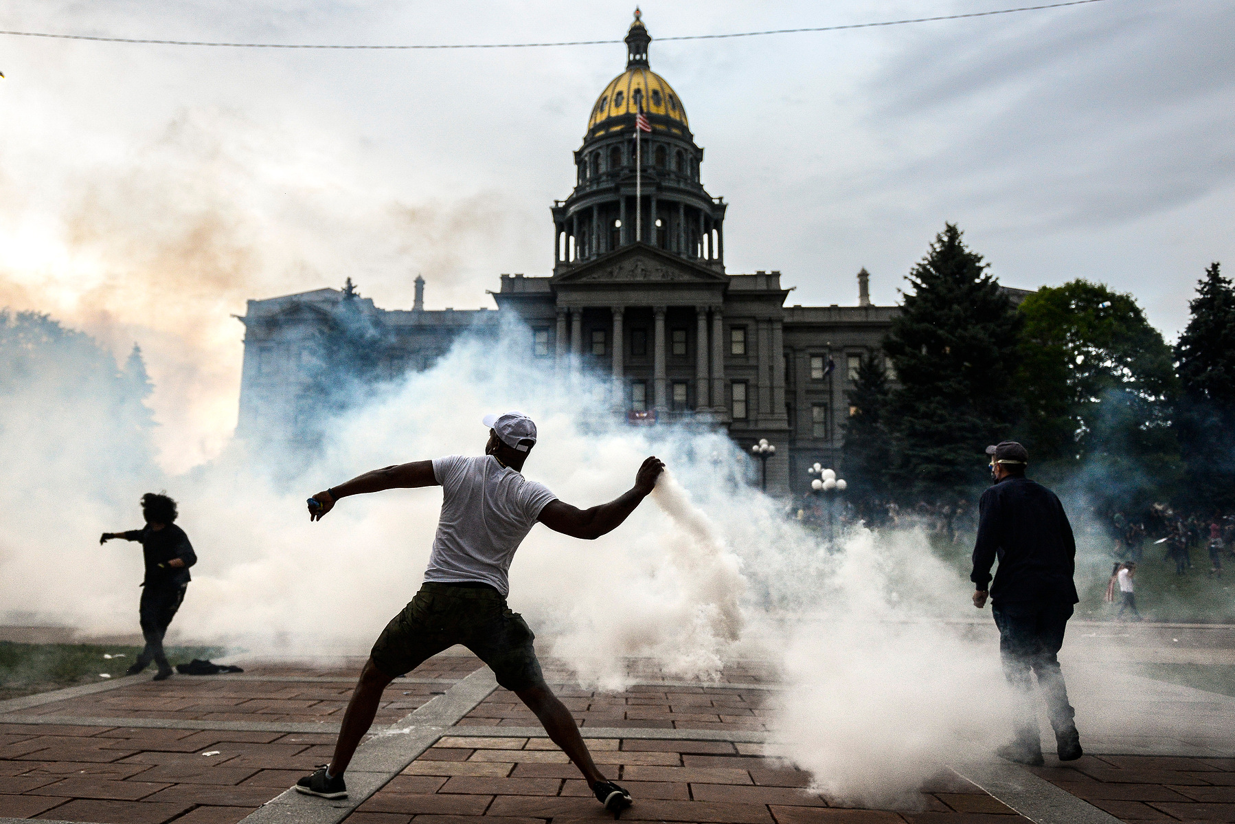 DENVER, CO - MAY 30: A man throws a tear gas canister back at police officers in front of the Colorado State Capitol as protests against the death of George Floyd continue for a third night on May 30, 2020 in Denver, Colorado. The city of Denver enacted a