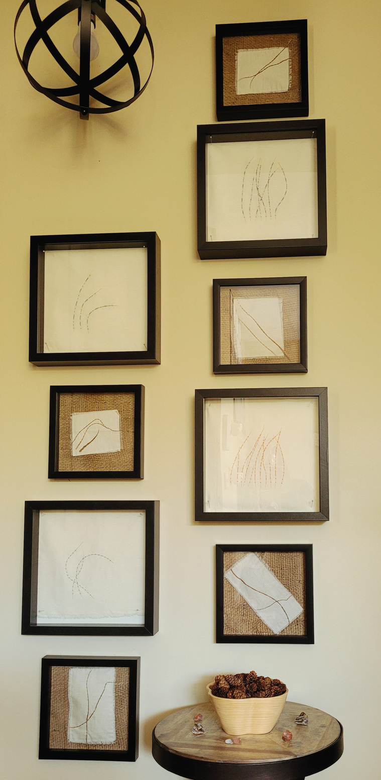 Natural Arrangements 2: This set of couched grasses embroidered onto muslin with various colors of fabrics and glass beads is mounted in black frames. The smaller pieces are stitched into burlap. The light fixture and small table are not included.