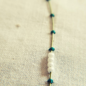 Art: One grass blade couched onto a cream fabric background with thick green thread and white glass beads