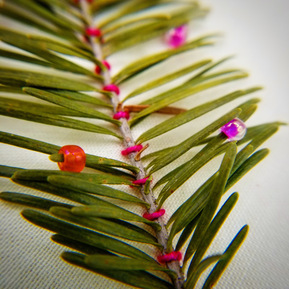 Art: Sprig of balsam fir couched onto a cream fabric background with thick pink thread and pink glass beads threaded onto the needles 