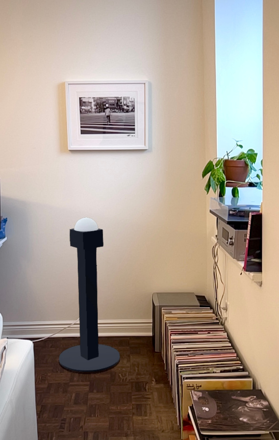 An augmented reality image of a three dimensionally rendered version of the cube stands under a photograph