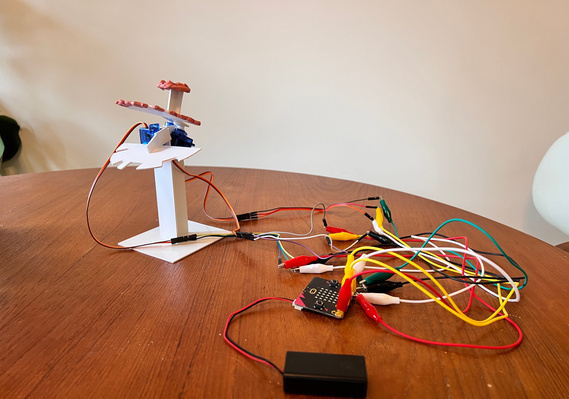 A series of colourful wires on a table that are connected to a Microbit and battery and a small plastic tower on the other.