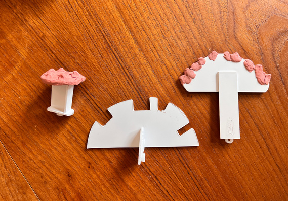 Three white plastic shapes on a table. Two semi circle and one with a flat top.