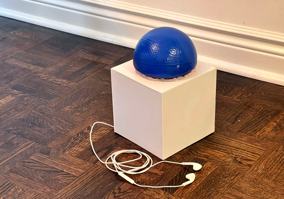 A white cube with a blue half rubber ball on top. white headphones come out of the left side and are wound up in front.