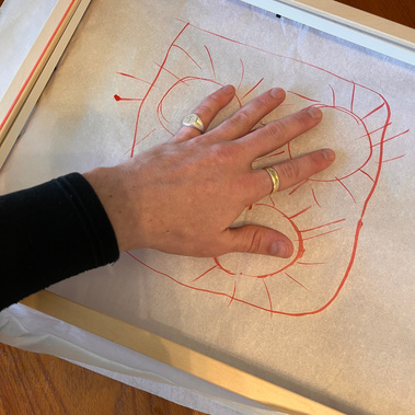 Hand with palm down against tissue paper that has been held around an empty frame. An abstract drawing on the paper.