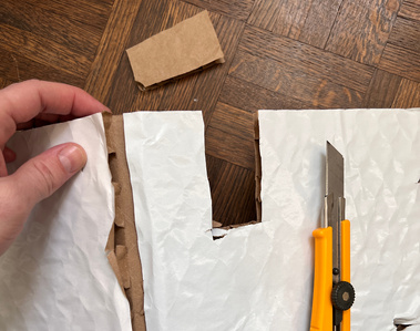 Rippled thick cardboard being cut with a yellow exact knife.