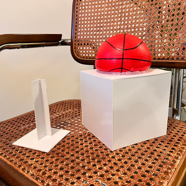 A toy basketball half glued to a white plastic cube, and a plastic T-beam standing straight up