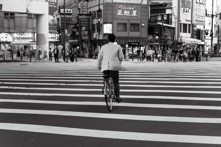Man riding bike across an intersection in Osaka with diagonal line as people wait on the opposite side