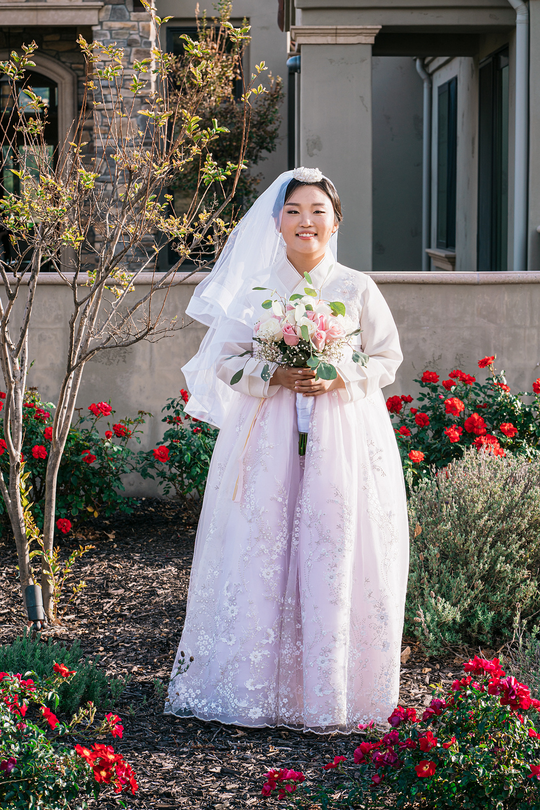 portrait of a smiling korean bride in hanbok standing among red flowers 