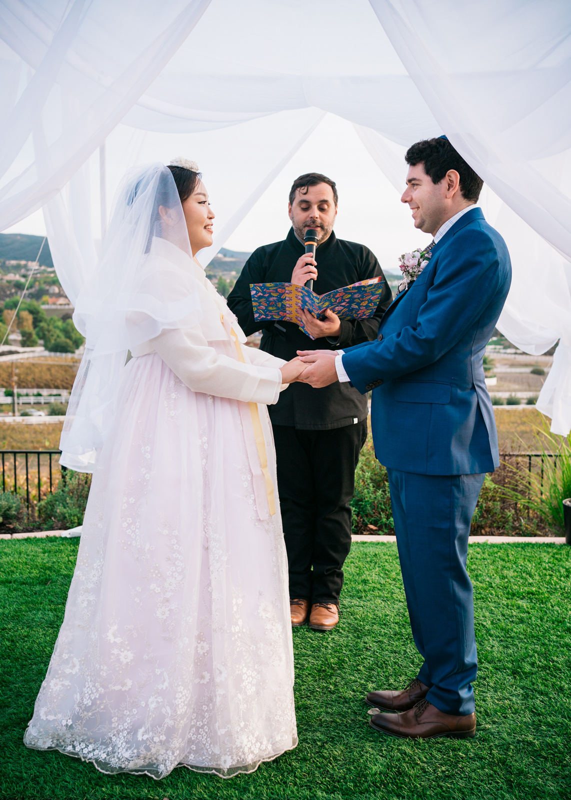 bride and groom holding hands looking into each others eyes while the officiant reads