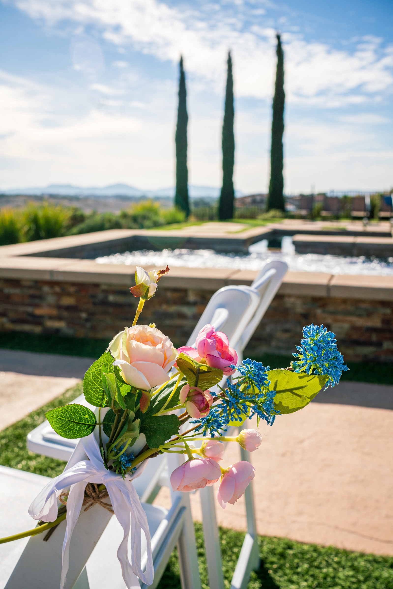 wedding flowers tied to a chair with the pool  cypress trees and blue skies in the background
