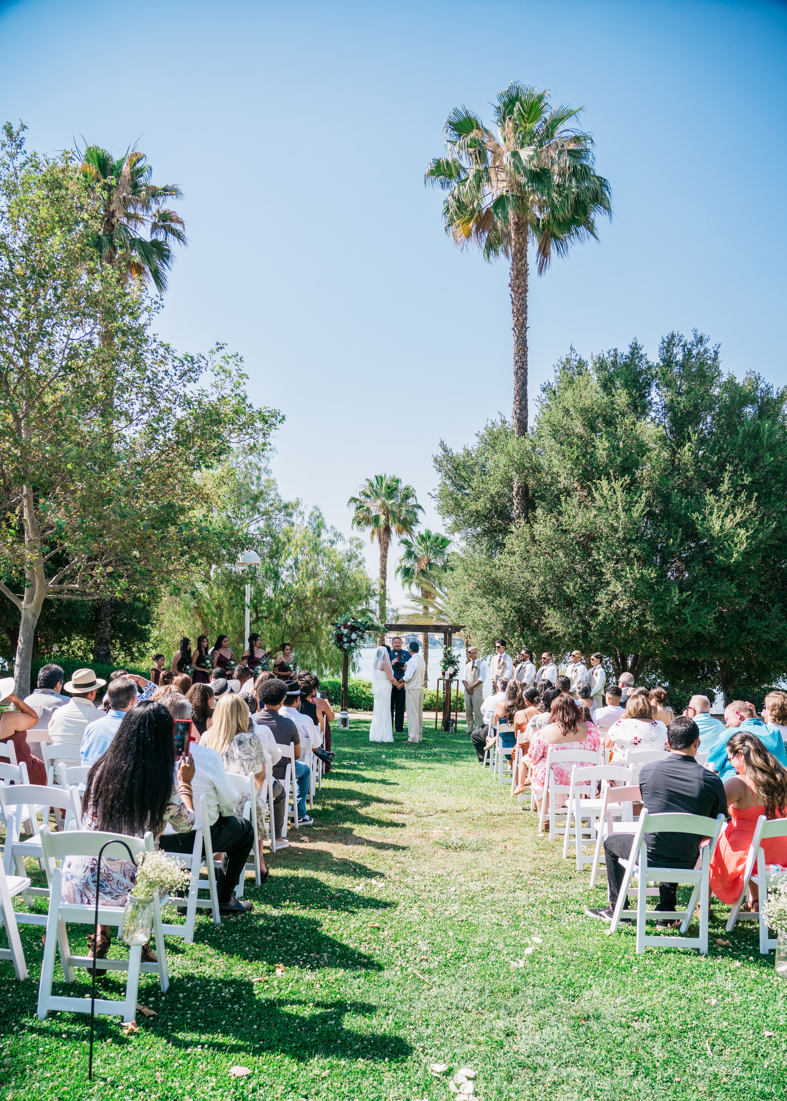 holiday harbor canyon lake wedding photographer the bride and groom with the pastor groomsmen and bridesmaid at the altar seated guests blue sky palm trees southern california wedding photographer