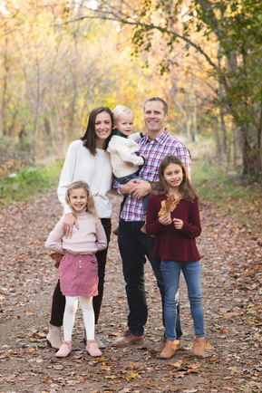 A photograph of a happy Family with three young children in a beautiful setting surrounded by colorful trees.