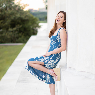 A girl laughing and leaning against the one of the columns at the Lincoln Memorial with the sun setting in the background.