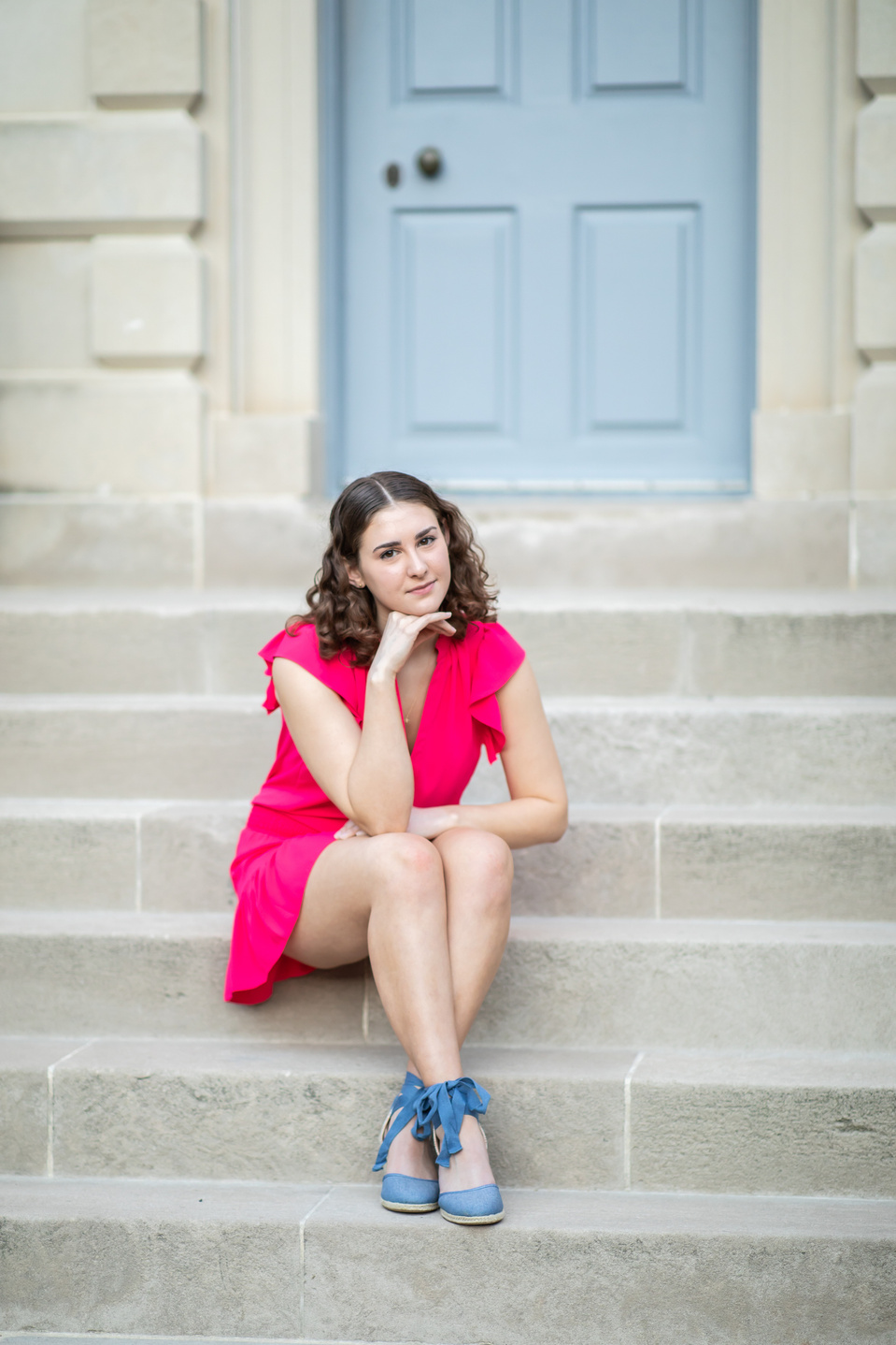 Teenage girl in a bright pink dress sat outside on stone steps leading to the pale blue front door of Carlyle House, Alexandria VA