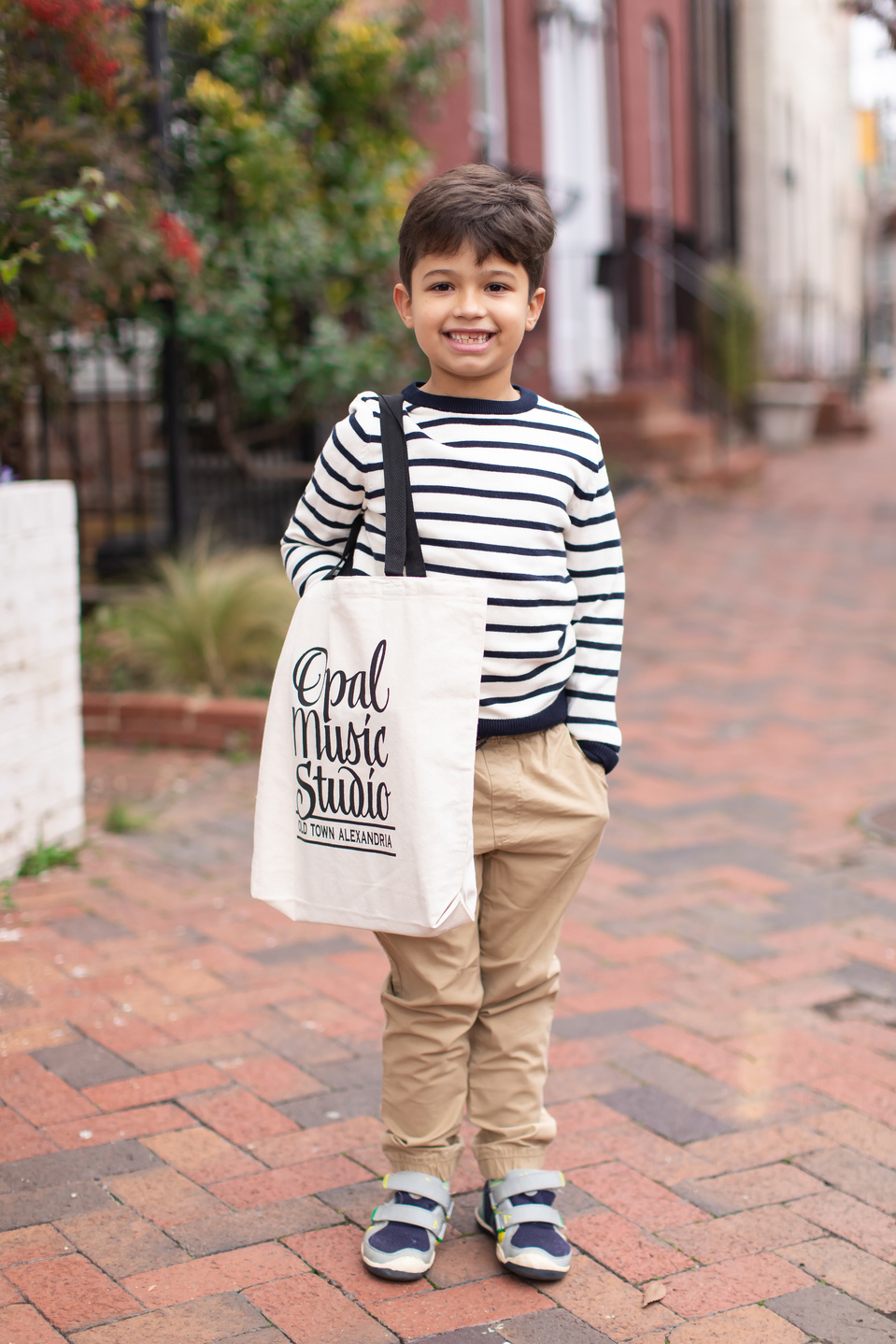 Small boy stood on a red brick street, with a Opal Music Studio tote bag on his shoulder.
