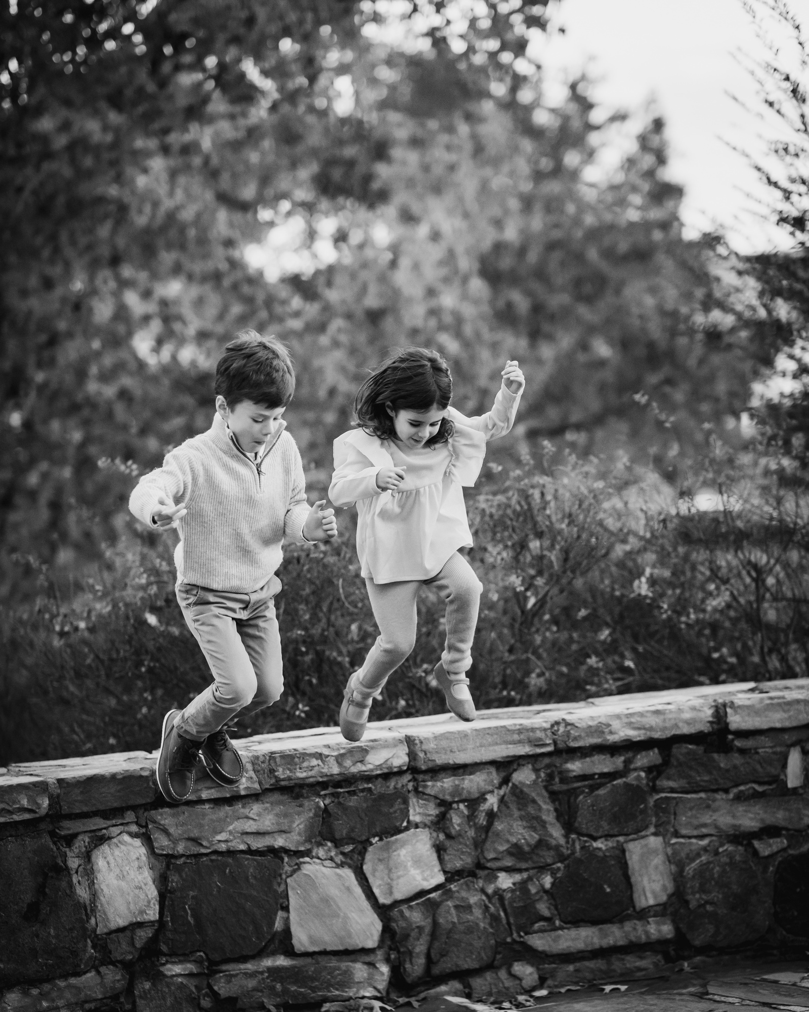 Two small children jumping off a wall at Windmill  park in Old Town Alexandria VA.