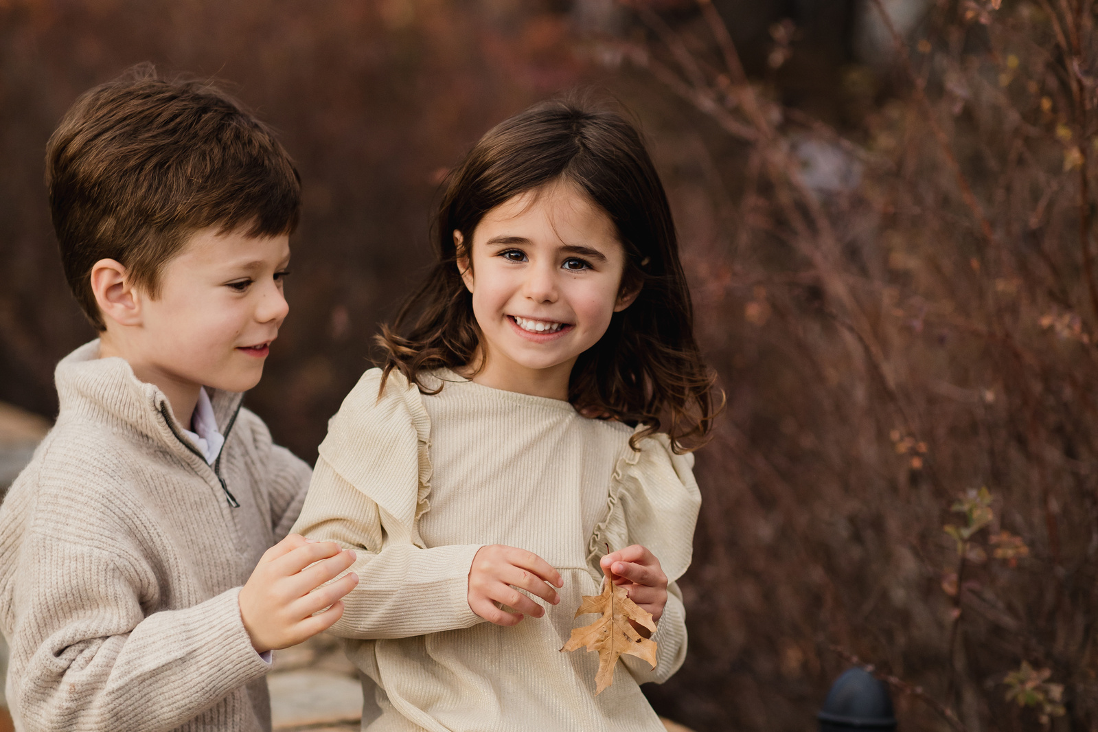 A  little boy and his sister with colorful trees and shrubs in the background.
