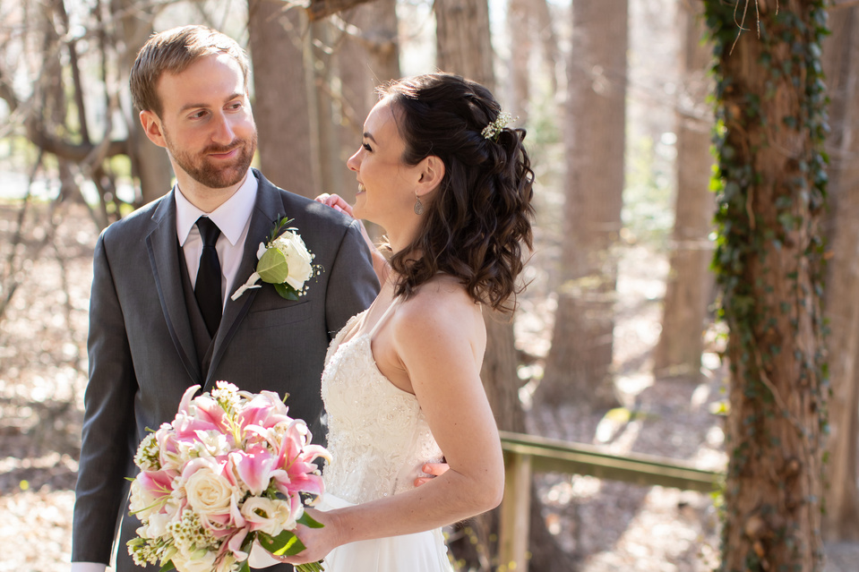 Bride and Groom looking at each other in a sun diffused wooded area.