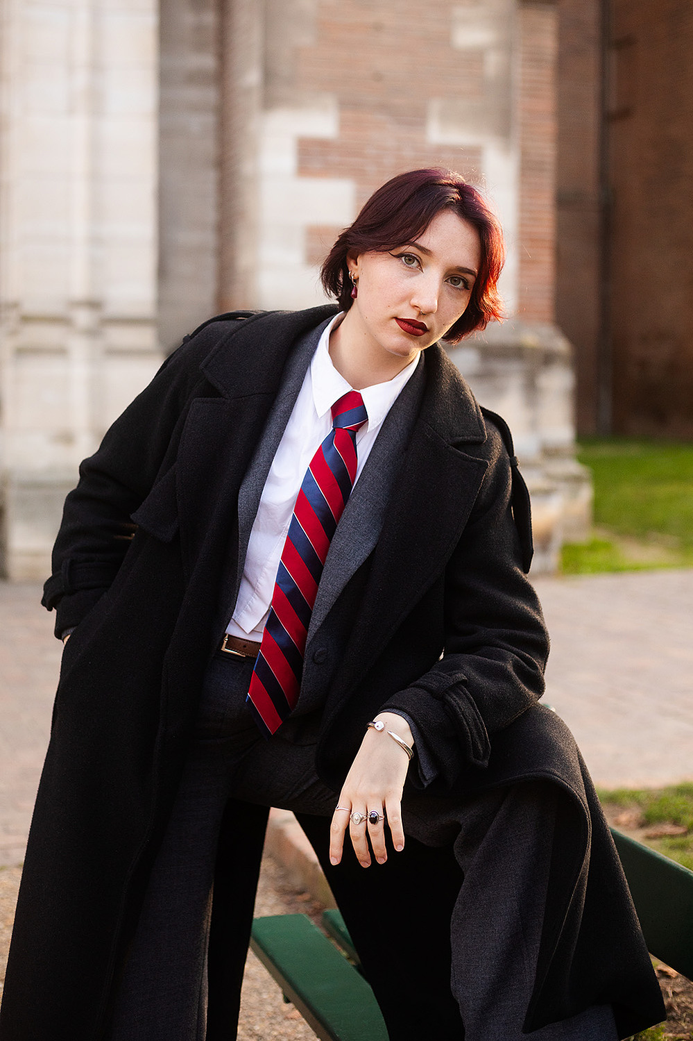 Portrait d'une jeune femme habillée en costume et cravate, accoudée contre un banc lors d'une séance photo à Toulouse.
