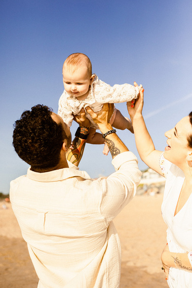 Des parents heureux qui porte leur bébé vers le ciel, sur une plage avec un ciel bleu.